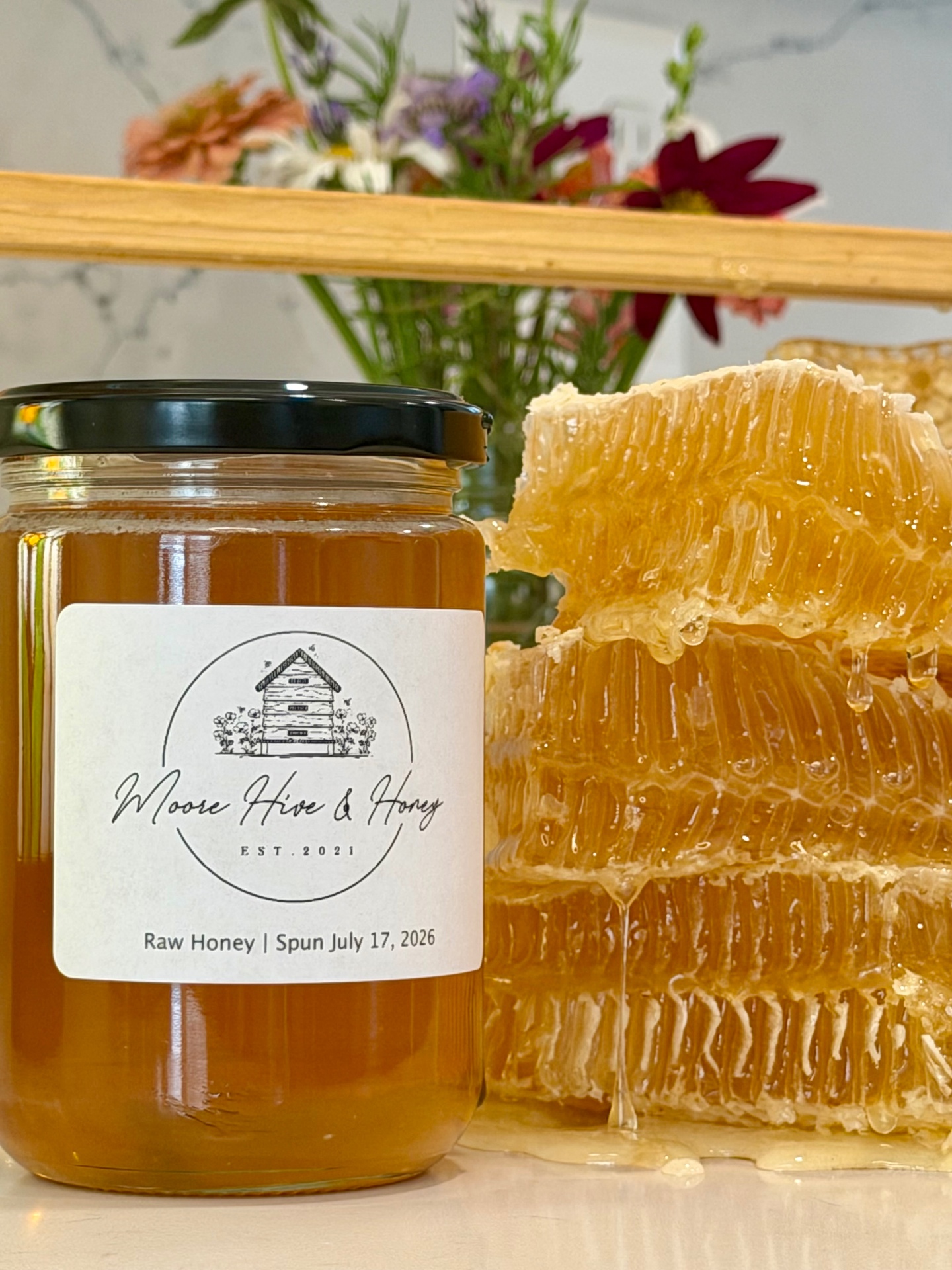 Jar of Moore Hive & Honey raw honey beside fresh honeycomb and wildflowers