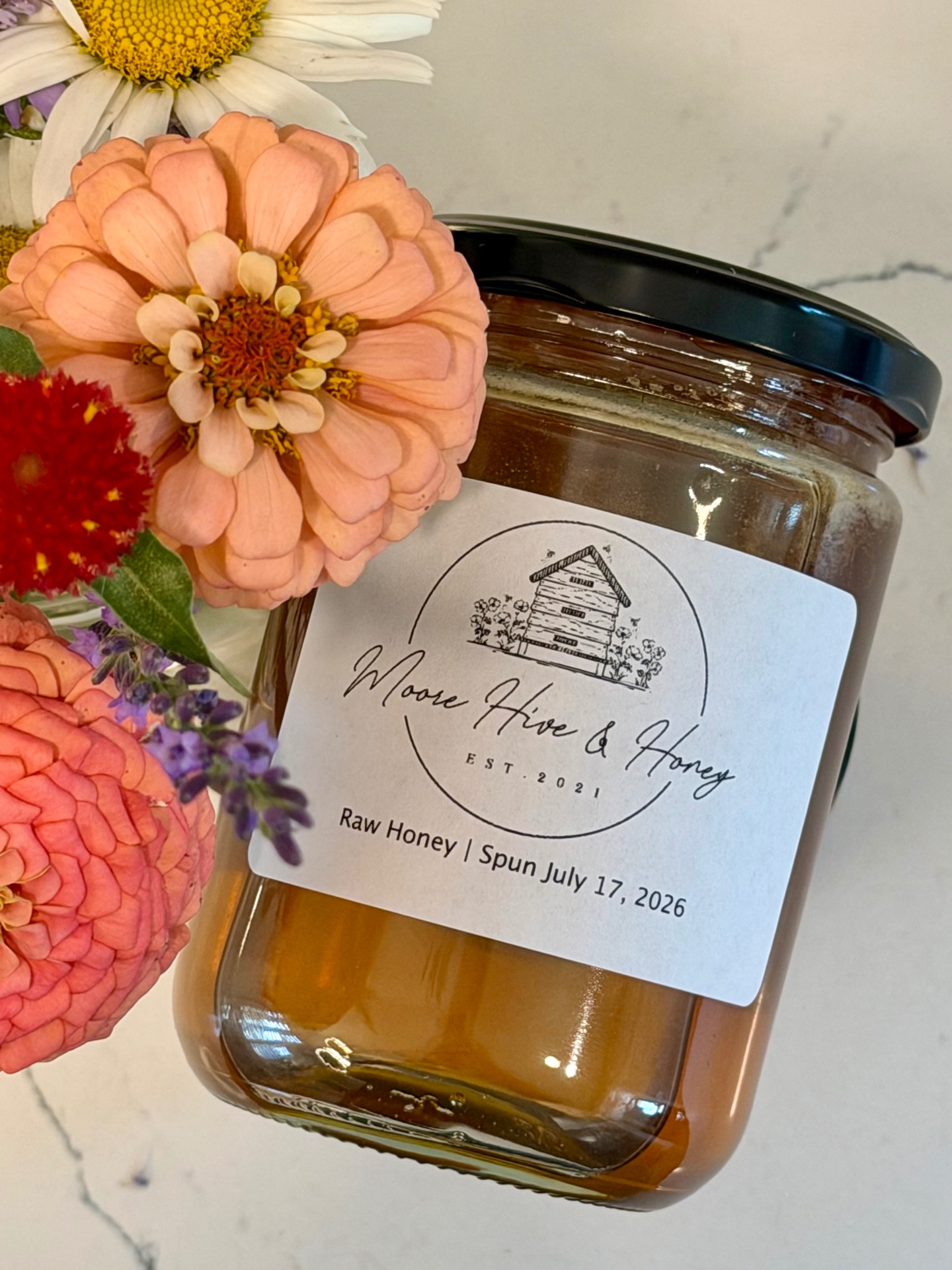 Close-up of a Moore Hive & Honey jar with zinnias and lavender